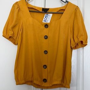 A yellow blouse w brown buttons lining the front.